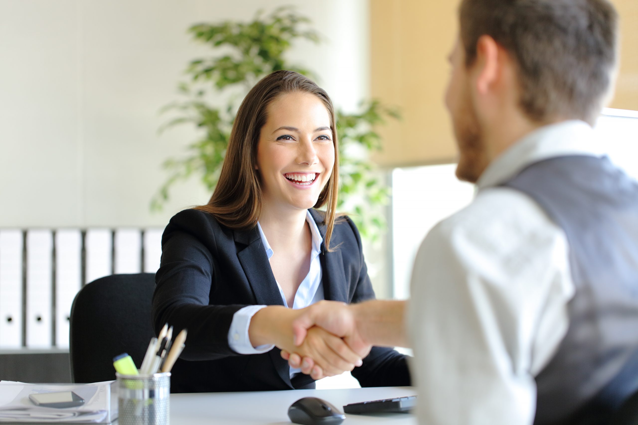 A professional shaking hands with a person across a desk in a bright office setting.