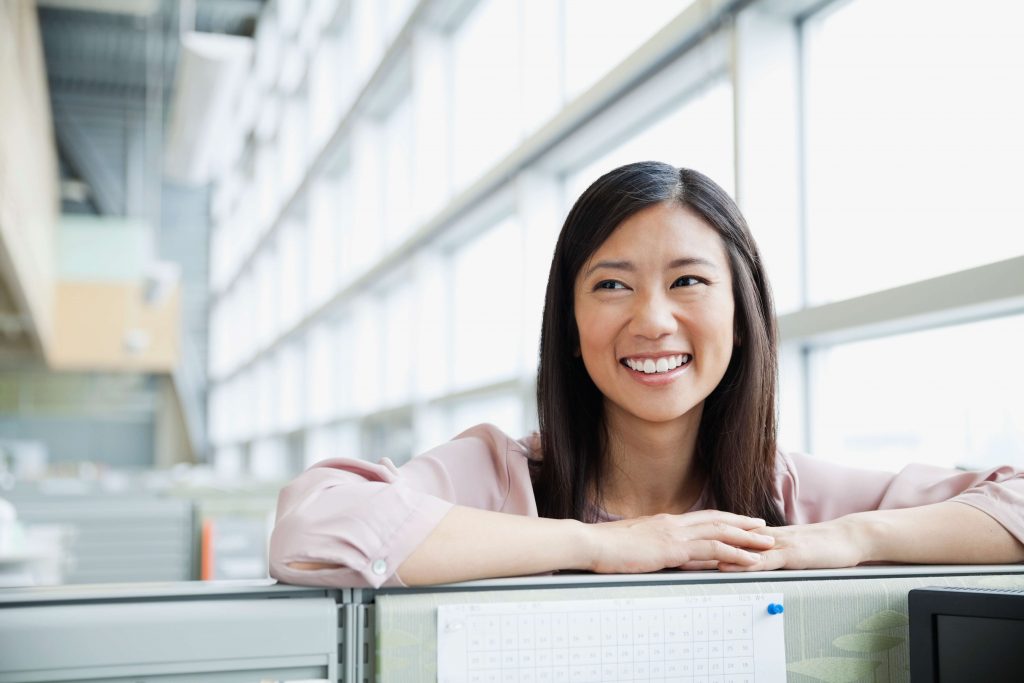 A cheerful person leans over a cubicle partition in a modern office.