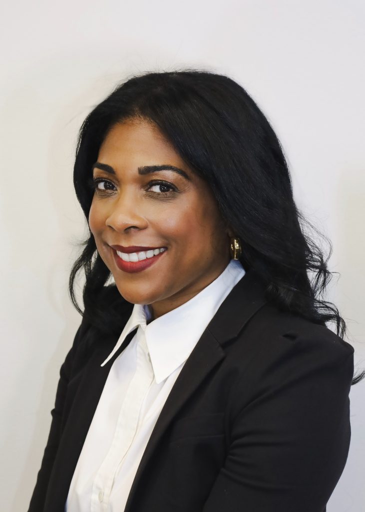 Professional portrait of a smiling woman with dark hair wearing a black blazer and white blouse against a light background, representing Human Resources.