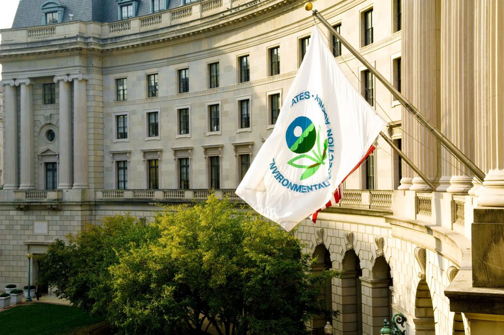 EPA flag flying in front of a grand government building with classical architecture and green trees.