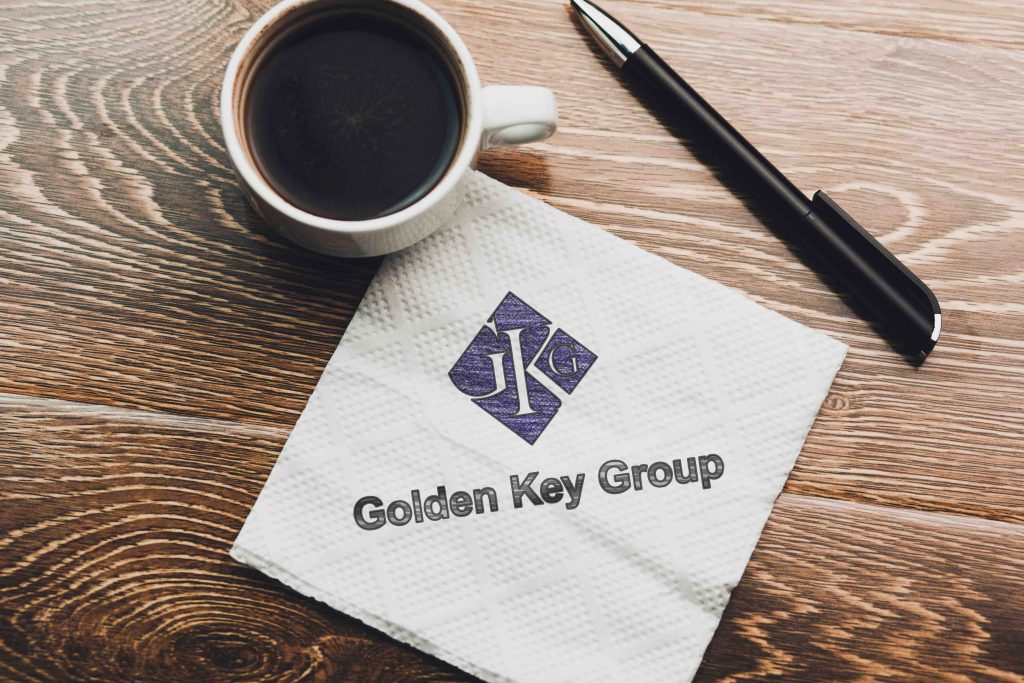 A coffee cup and pen resting on a napkin with "Golden Key Group" logo on a wooden table surface.