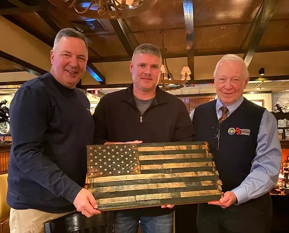 Three men holding a rustic American flag inside a warmly lit restaurant, discussing Workforce Optimization strategies.