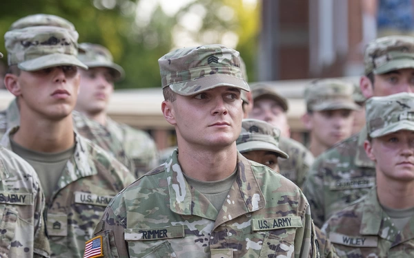Group of U.S. Army soldiers standing in uniform, with focus on a soldier in the foreground, looking intently forward.