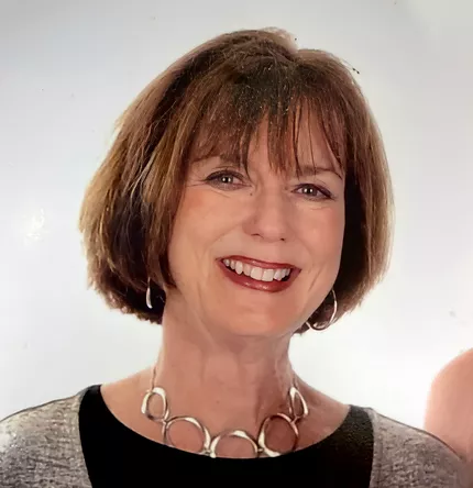 A smiling middle-aged woman with short brown hair, specializing in Human Resources, wearing a silver necklace and a gray and black top.