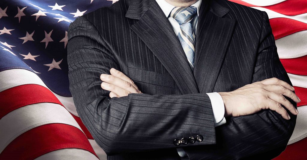 Businessperson in a suit crossing arms in front of an American flag, symbolizing Professional Consulting Services.